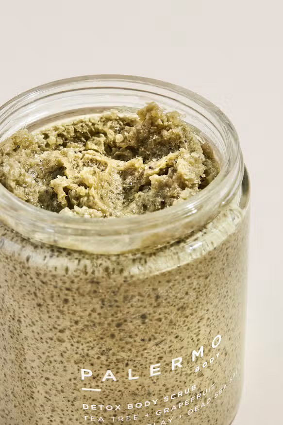 A glass jar of Palermo Body's Tea Tree and Grapefruit Body Scrub with a black lid contains 8.5 oz (240 g) of a grainy, moisturizing mixture. The label reads "Palermo Body Detox Body Scrub Tea Tree + Grapefruit with Sea Clay + Dead Sea Salt.
