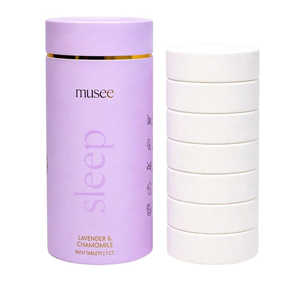 A hand wearing a gold bracelet places a MUSEE - SLEEP BATH TABLET into a tub of water, releasing gentle bubbles that rise to the surface. Green leaves in the corner highlight the natural ingredients in this bath product from MUSEE.
