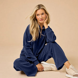 A woman seated on the floor wearing a Softies - Serenity 1/4 Zip Top with Wide Leg Pant lounge set in midnight, featuring a navy blue quarter-zip pullover and matching wide-leg lounge pants.