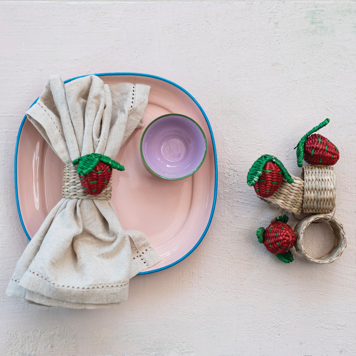 The CREATIVE COOP HAND-WOVEN SEAGRASS STRAWBERRY NAPKIN RINGS, SET OF 4, feature red and green strawberry accents and are displayed on a white background.