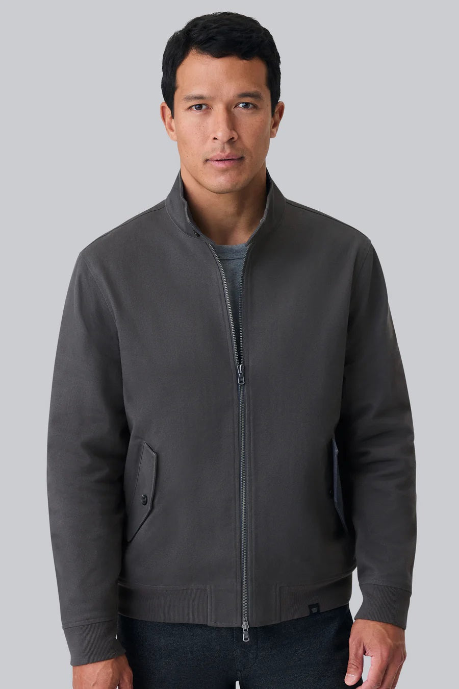 The MACK WELDON Twill Harrington Jacket in Asphalt is a dark gray cotton cavalry twill zip-up with a stand collar, two angled button-flap pockets, ribbed cuffs and hem, offering an English jacket style. Shown on a black background.