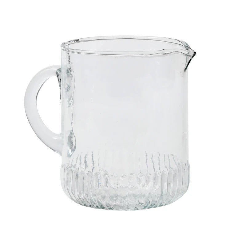 The ETUHOME - BISTRO GLASS MINI JUG by ETUHOME, filled with milk, rests on a white surface next to a butter dish and knife, with a clear glass baking dish and wooden container in the background.