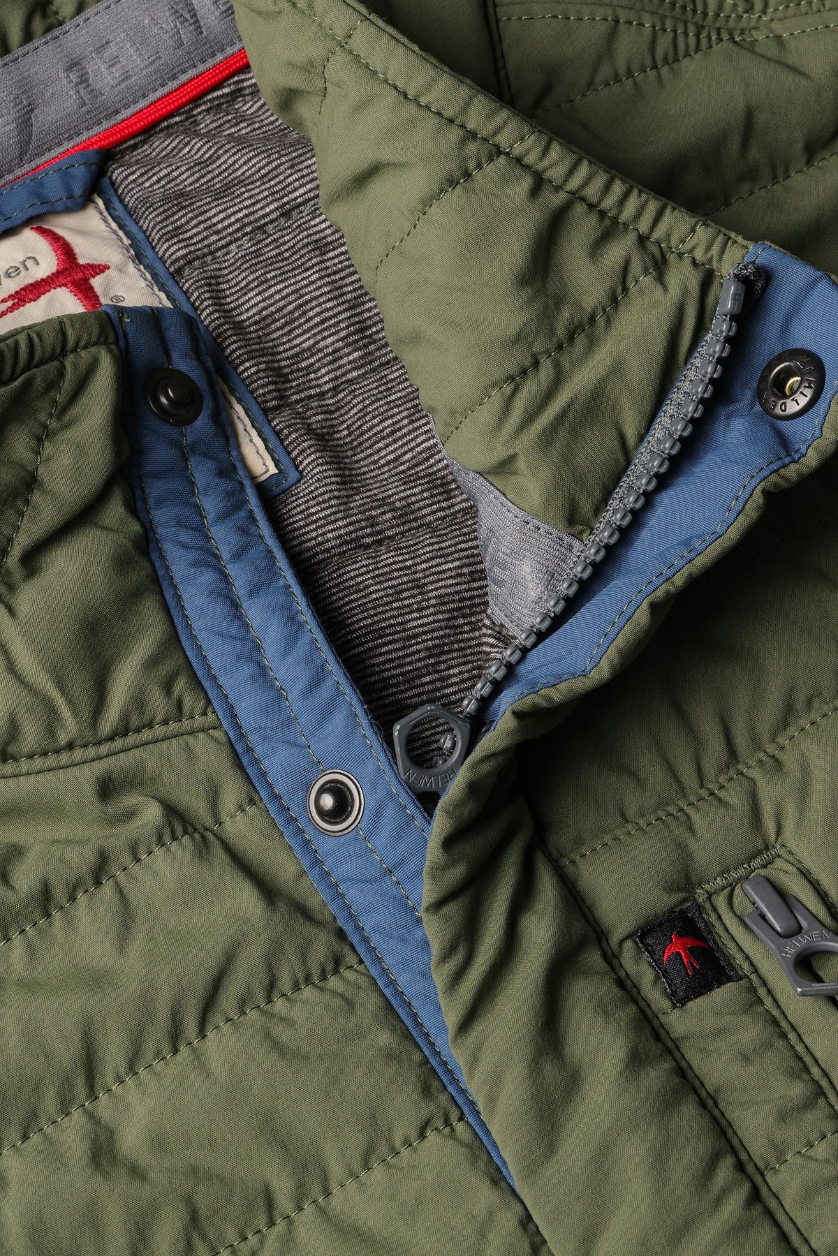 The RELWEN Windzip Vest in Olive is a quilted utility vest with green and blue trim, snap button closures, armholes, and an inner pocket—ideal for layered warmth. Shown open and laid flat.