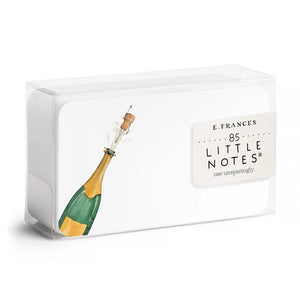 A clear box holds 85 E. FRANCES PAPER - FLYING CORK LITTLE NOTES—small, hand painted notecards from E. FRANCES PAPER, featuring a champagne bottle "flying cork" design. The label reads "E. Frances 85 Little Notes—use unsparingly.