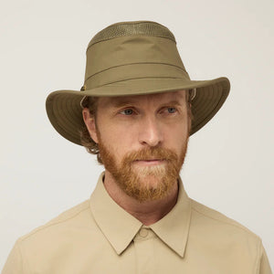 A man with a red beard and wavy hair, wearing a tan button-up shirt and a TILLEY AIRFLO Medium Brim LTM5 hat by TILLEY, is shown in profile against a plain light background.