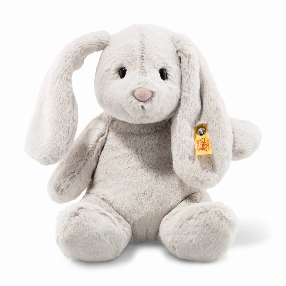 The STEIFF - HOPPIE RABBIT is an upright plush toy bunny with light gray fur, long floppy ears, and a simple embroidered face featuring a small pink nose. It includes the classic yellow Steiff tag on its left ear.