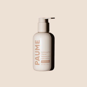 A person dispenses foam from a white PAUME - EXFOLIATING HAND SOAP bottle onto their hand under a sink. Text highlights it's free of parabens, sulfates, and silicones, with icons for vegan, cruelty-free, natural, and sustainable.