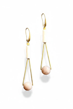 The DAVID AUBREY - PEACH MOONSTONE GEOMETRIC EARRINGS by DAVID AUBREY feature a sleek 18k gold plated triangular wire design, adorned with a white magnesite cylindrical bead at the top and a round peach moonstone bead at the bottom, showcased against a gray background.