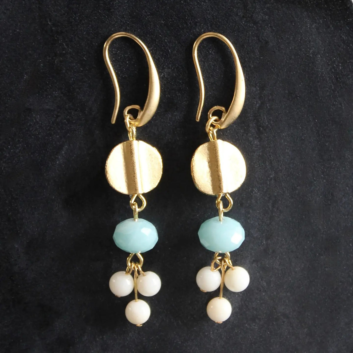 The DAVID AUBREY - AMAZONITE AND GLASS EARRINGS by DAVID AUBREY feature a round gold disk, a light blue amazonite bead, and three small white glass beads hanging from each earring, creating an elegant blend of classic style and contemporary charm against a striking black background.