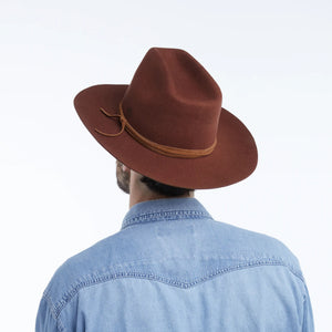 The WYETH Costa Cowboy Hat in Cinnamon features a wide brim, pinched crown, and thin suede trim tied in a bow. This adjustable hat by WYETH is shown on a white background.