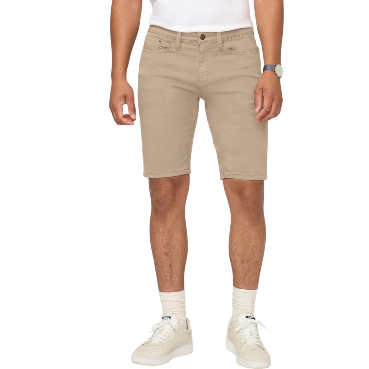A person wearing a white t-shirt, DUER No Sweat Relaxed Shorts in Desert Khaki, white crew socks, white sneakers, and a wristwatch stands against a plain light background.