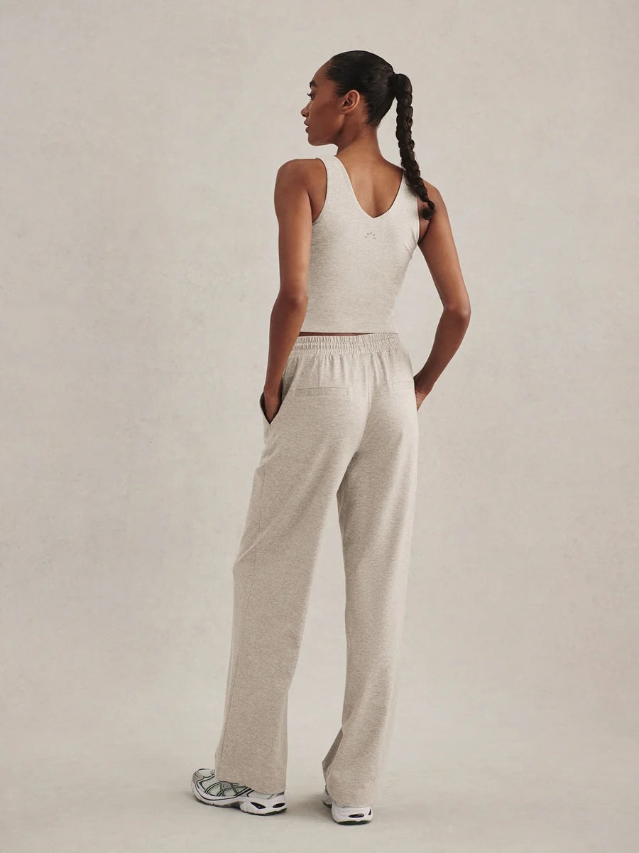 A woman wearing a light gray Varley Motion Easy Jogger 30 in Pebble Marl tank top and matching wide-leg joggers with athletic shoes.