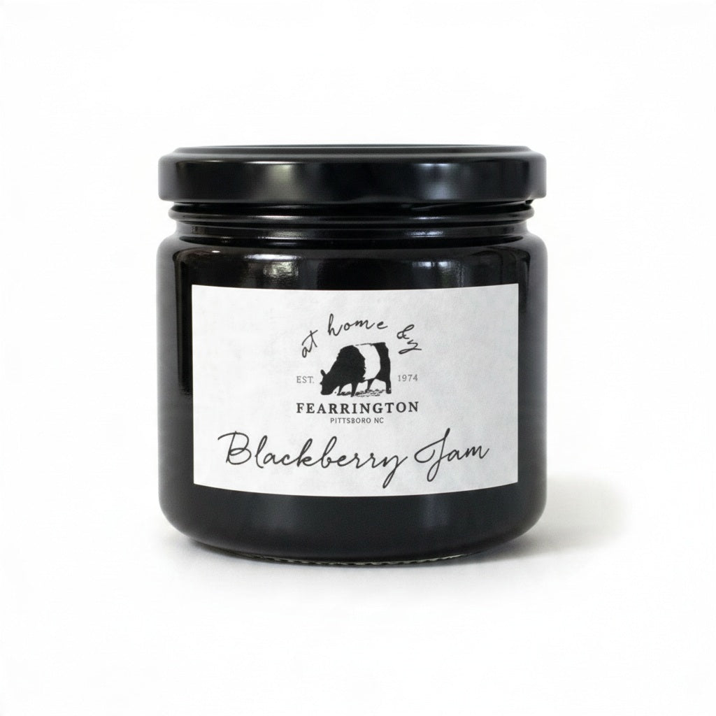 The FEARRINGTON SIGNATURE COLLECTION - FEARRINGTON HOUSEMADE BLACKBERRY JAM features a stylish black and white striped ribbon tied around the lid. The label reveals ingredients including blackberry, vanilla, lemon, pectin, and sugar. This handcrafted jam is made with meticulous care and is an ideal hostess gift. Please be aware that it may contain allergens.