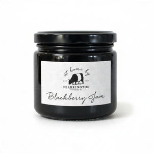 The FEARRINGTON SIGNATURE COLLECTION - FEARRINGTON HOUSEMADE BLACKBERRY JAM features a stylish black and white striped ribbon tied around the lid. The label reveals ingredients including blackberry, vanilla, lemon, pectin, and sugar. This handcrafted jam is made with meticulous care and is an ideal hostess gift. Please be aware that it may contain allergens.