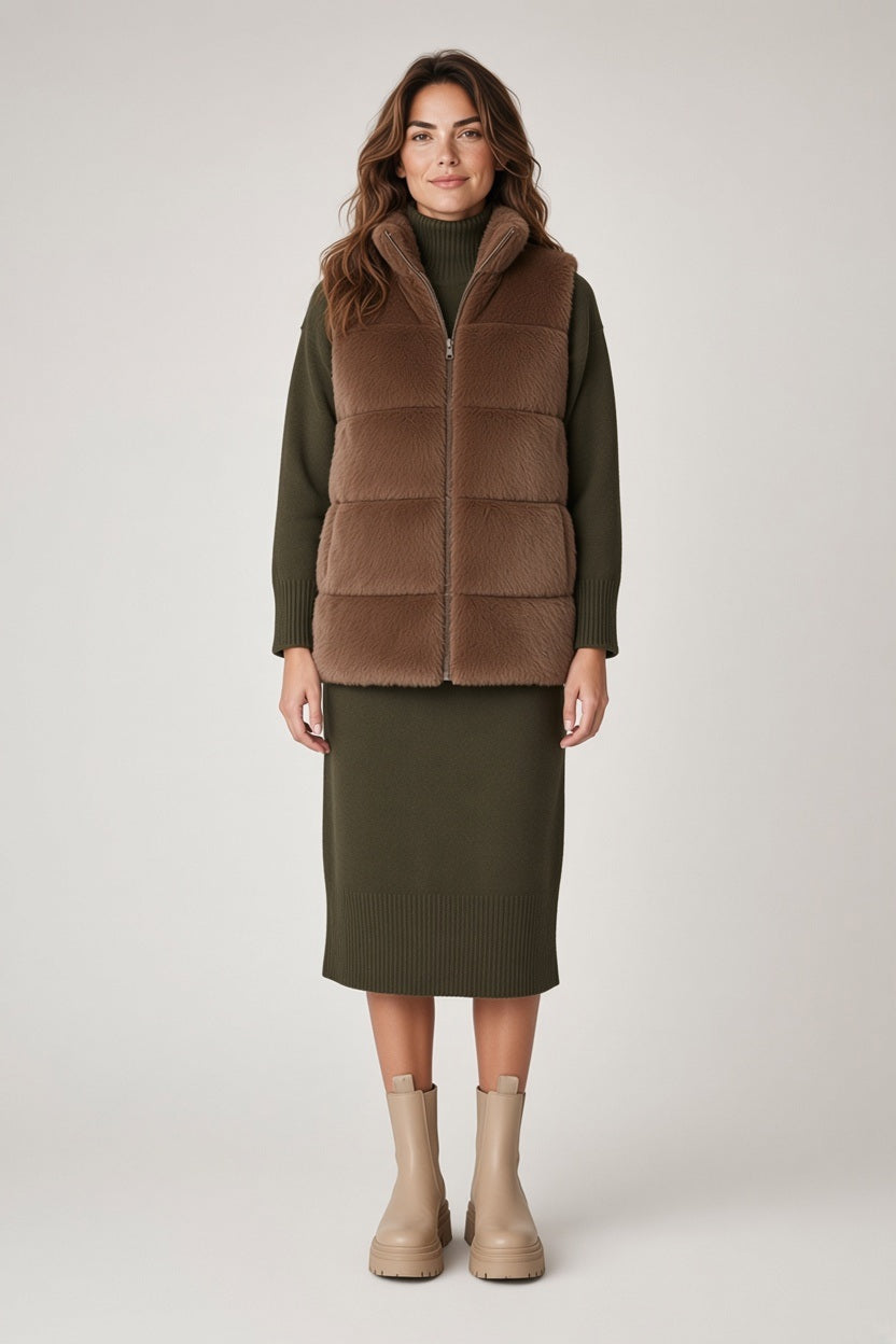 A model wearing a SAVE THE DUCK - NIVES REVERSIBLE FAUX FUR VEST IN NOISETTE BROWN over an olive green sweater dress and beige boots.