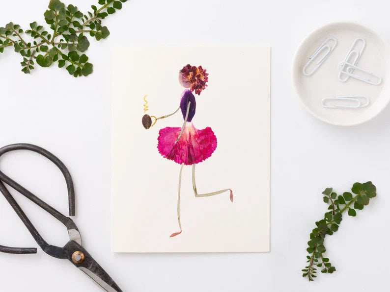 The PETAL PEOPLE PRESS - CUP O&#39; JOE CARD by PETAL PEOPLE PRESS features a floral figure gracefully dancing in a pink petal skirt and purple top, crowned with a carnation. The figure holds a small spiral object, with limbs made of leaf stems—ideal for notecard designs.