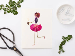 The PETAL PEOPLE PRESS - CUP O' JOE CARD by PETAL PEOPLE PRESS features a floral figure gracefully dancing in a pink petal skirt and purple top, crowned with a carnation. The figure holds a small spiral object, with limbs made of leaf stems—ideal for notecard designs.