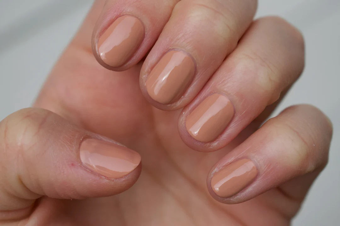 A glass bottle of TENOVERTEN - NAIL POLISH from the brand TEN OVER TEN, featuring a white cap and a dusty pink nail color. The front label displays "TEN OVER TEN" in white uppercase letters. This vegan, eight-free formula ensures both beauty and peace of mind. The background is plain and light-colored.