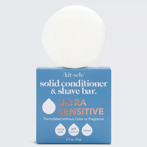 A white, multi-purpose solid conditioner and shave bar sits on a blue box labeled "KITSCH - ULTRA SENSITIVE CONDITIONER & SHAVE BAR." Formulated without color or fragrance, it features icons indicating it's color safe, pH balanced, vegan, and environmentally friendly.