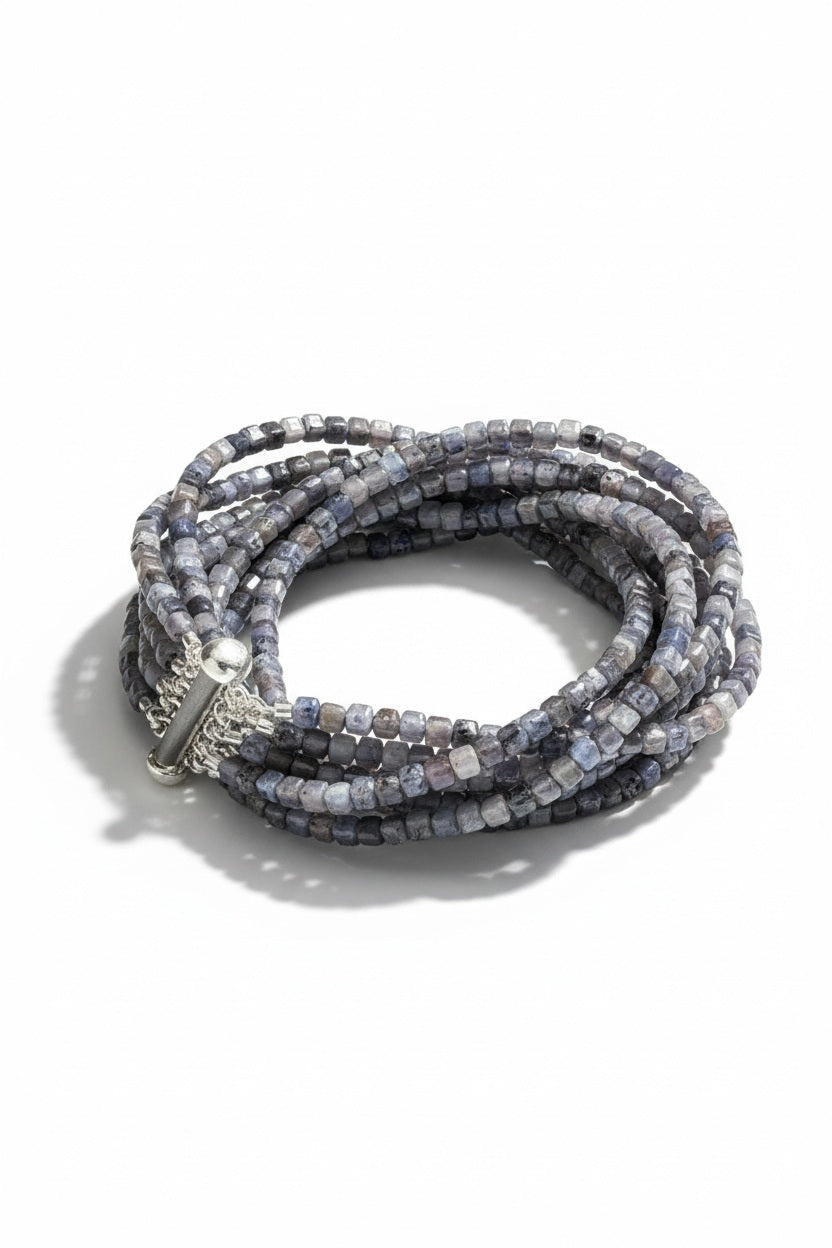 The ANN LIGHTFOOT Iolite Squares Ten Strand Bracelet features multiple strands of small, faceted square-cut blue and gray iolite beads with a silver slide clasp, shown against a white background.
