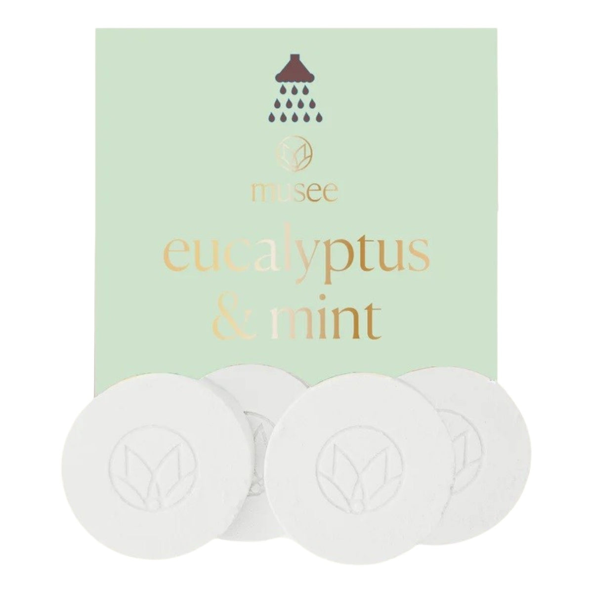 A pastel green packet labeled “MUSEE - EUCALYPTUS &amp; MINT SHOWER STEAMERS” from MUSEE, featuring a shower icon, is displayed behind four round white shower steamers embossed with a leaf design—offering a spa-like experience with these natural bath products.