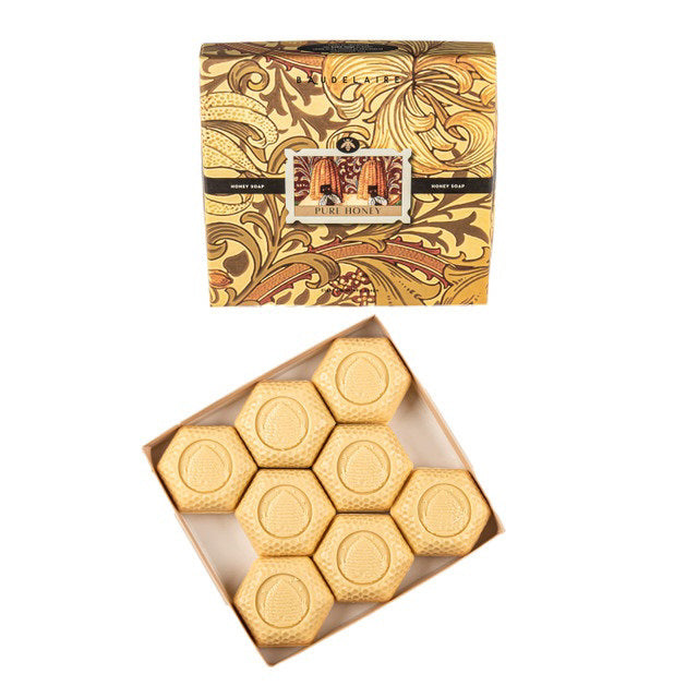 A decorative box from BAUDELAIRE labeled &quot;Pure Honey Soap&quot; reveals eight hexagonal bars of soap arranged in neat rows. These 1.4 oz. bars, each carefully triple-milled and featuring embossed designs, perfectly echo the honeycomb theme presented on the packaging.