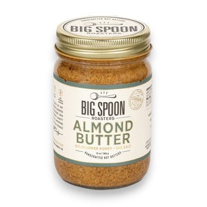 A jar of BIG SPOON ROASTERS Almond Butter with a golden lid. The label reads: "Handcrafted Nut Butter," "BIG SPOON ROASTERS - ALMOND BUTTER WILDFLOWER HONEY NUT BUTTER," "With Organic Wildflower Honey & Sea Salt," and "12 oz." Featuring heirloom Mission almonds, the label boasts a spoon illustration and other decorative elements.