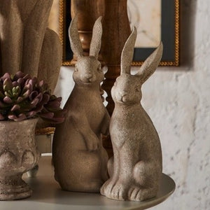 The RAZ IMPORTS RABBIT WITH BOW features two upright, concrete-look rabbit figurines with textured surfaces and yellow or green bows—charming rustic décor accents for any space.