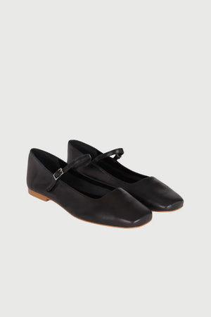 The AUGUSTA - JULIETA MARY JANE by AUGUSTA is a black leather flat shoe featuring a slender, adjustable strap across the top and a low wooden heel. With its renewed silhouette, slightly pointed toe, and minimalist design, this handcrafted Spanish shoe is presented against a plain, light gray background.