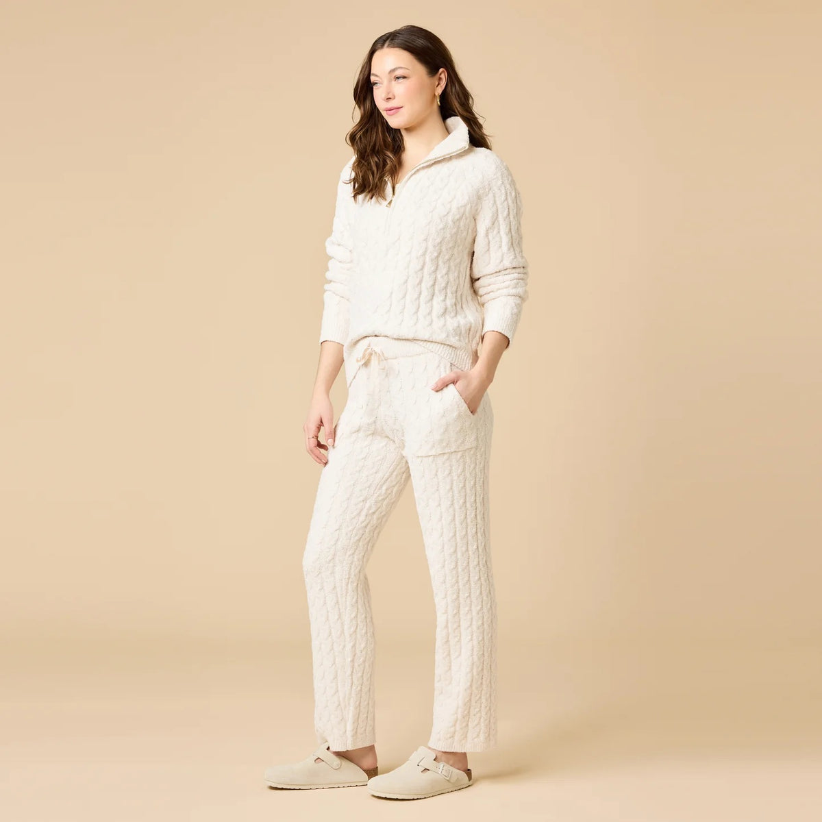 A woman wearing a marshmallow-soft, cream-colored SOFTIES - CABLE KNIT MARSHMALLOW ½ ZIP WITH TAPERED PANT SET, featuring a half-zip pullover and matching pants with a drawstring waist.