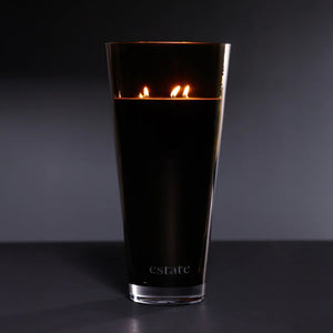 A collection of ZODAX luxury scented candles, including the 57 OZ THISTLE ESTATE CANDLE in black and smoky brown, is displayed on a white textured surface against a plain light background.