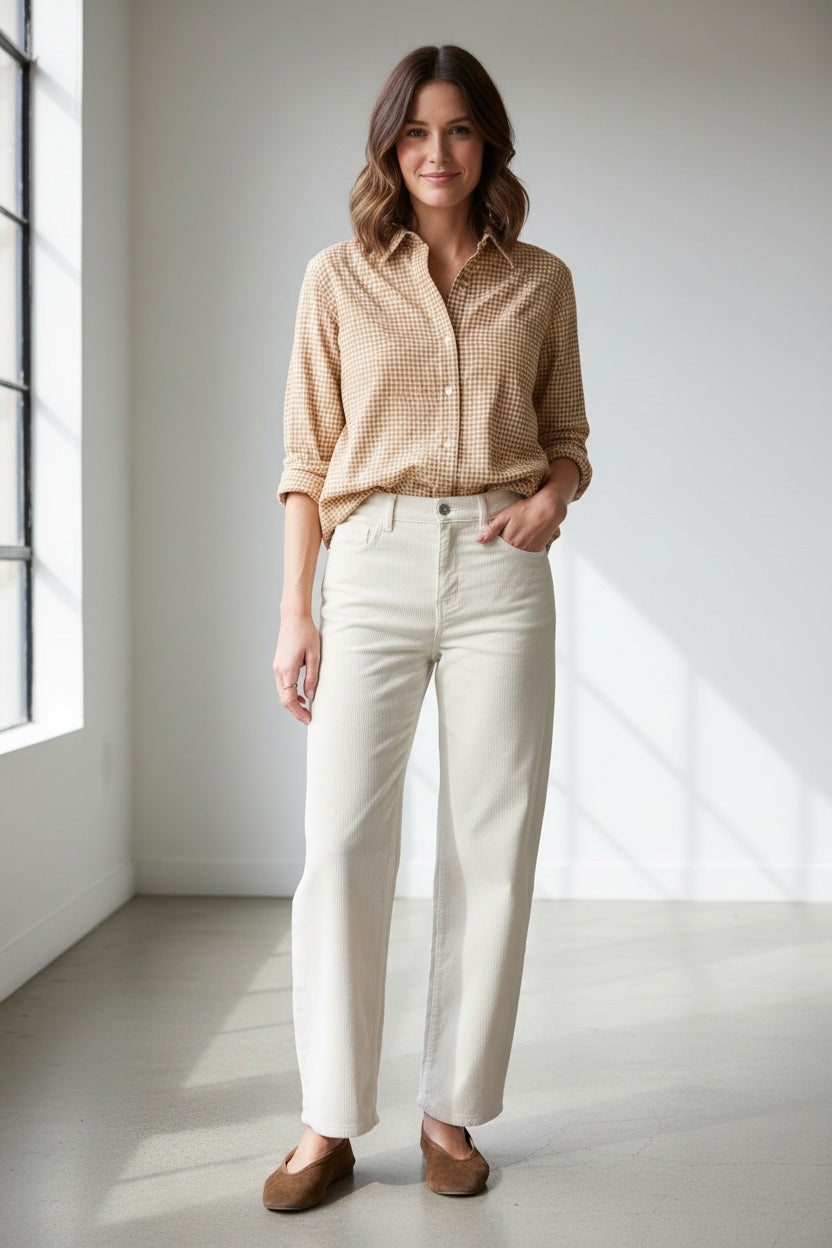 A woman wearing a tan and white gingham button-down shirt tucked into FRANK AND EILEEN - BRENNAN EVERYDAY BARREL IN ITALIAN PERFORMANCE CORDUROY VINTAGE WHITE barrel jeans.