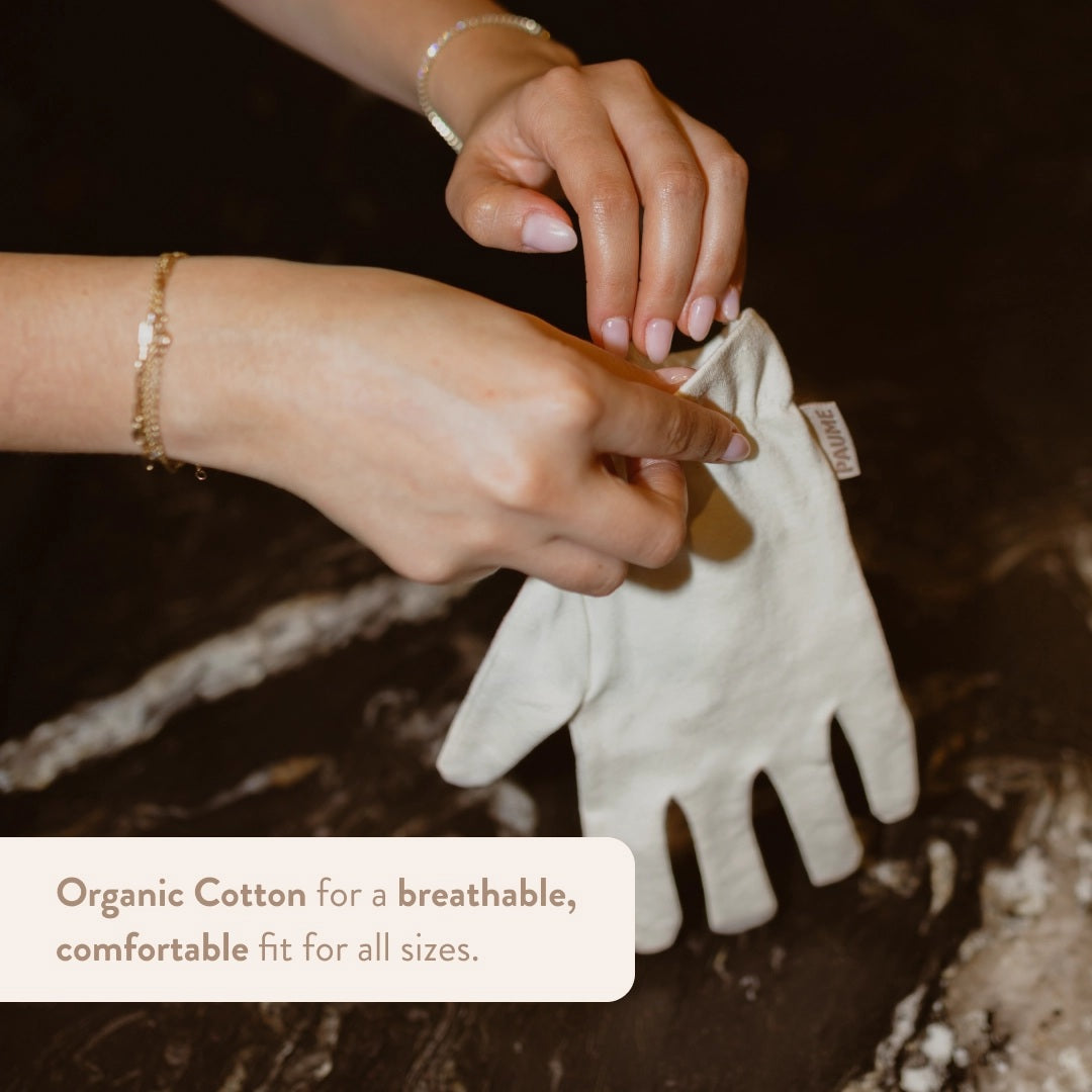 PAUME - ORGANIC COTTON OVERNIGHT GLOVES by PAUME are soft, off-white gloves with a subtle sheen, elastic wrists, and a simple design. Made from organic cotton, they’re perfect for nighttime moisturizing and shown on a matching beige background.