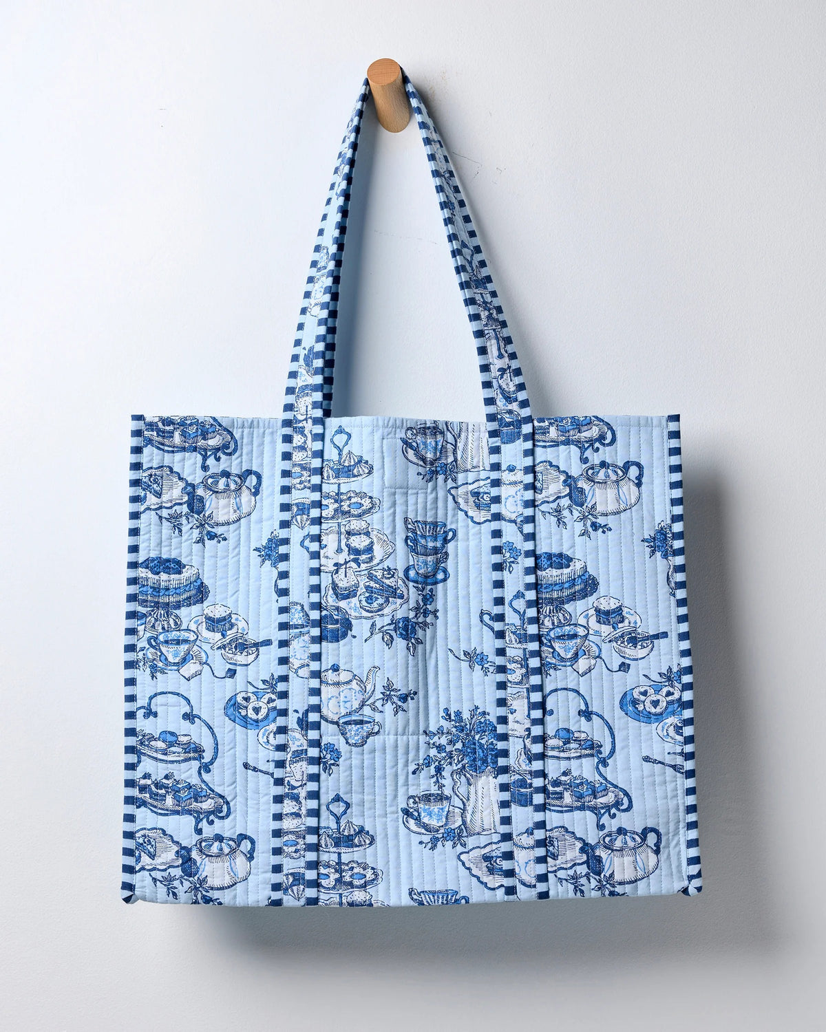 Smiling woman in a white shirt carries the spacious PRINTFRESH - HIGH TEA TOILE TRAVELER TOTE, featuring a bold blue-and-white pattern and draped over her shoulder as she stands against a plain light background—the perfect organic cotton tote bag from PRINTFRESH for the tea lover gift in your life.