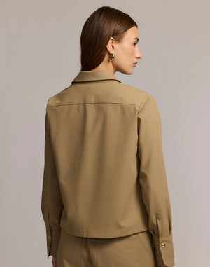 A woman with long brown hair wears the HINSON WU - ASTRID LONG SLEEVE TRAVELER'S TWILL SHIRT JACKET over a black top and tan pants. She stands against a light background, looking confidently at the camera.