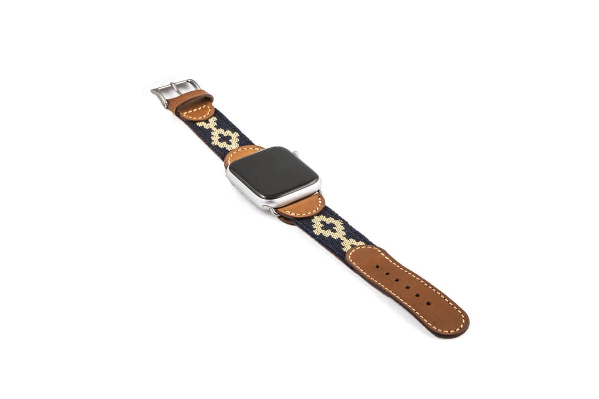 The LA MATERA - CORBINA Apple Watch Band in silver pairs artisan brown leather with a black fabric section, beige geometric pattern, and red stitching.