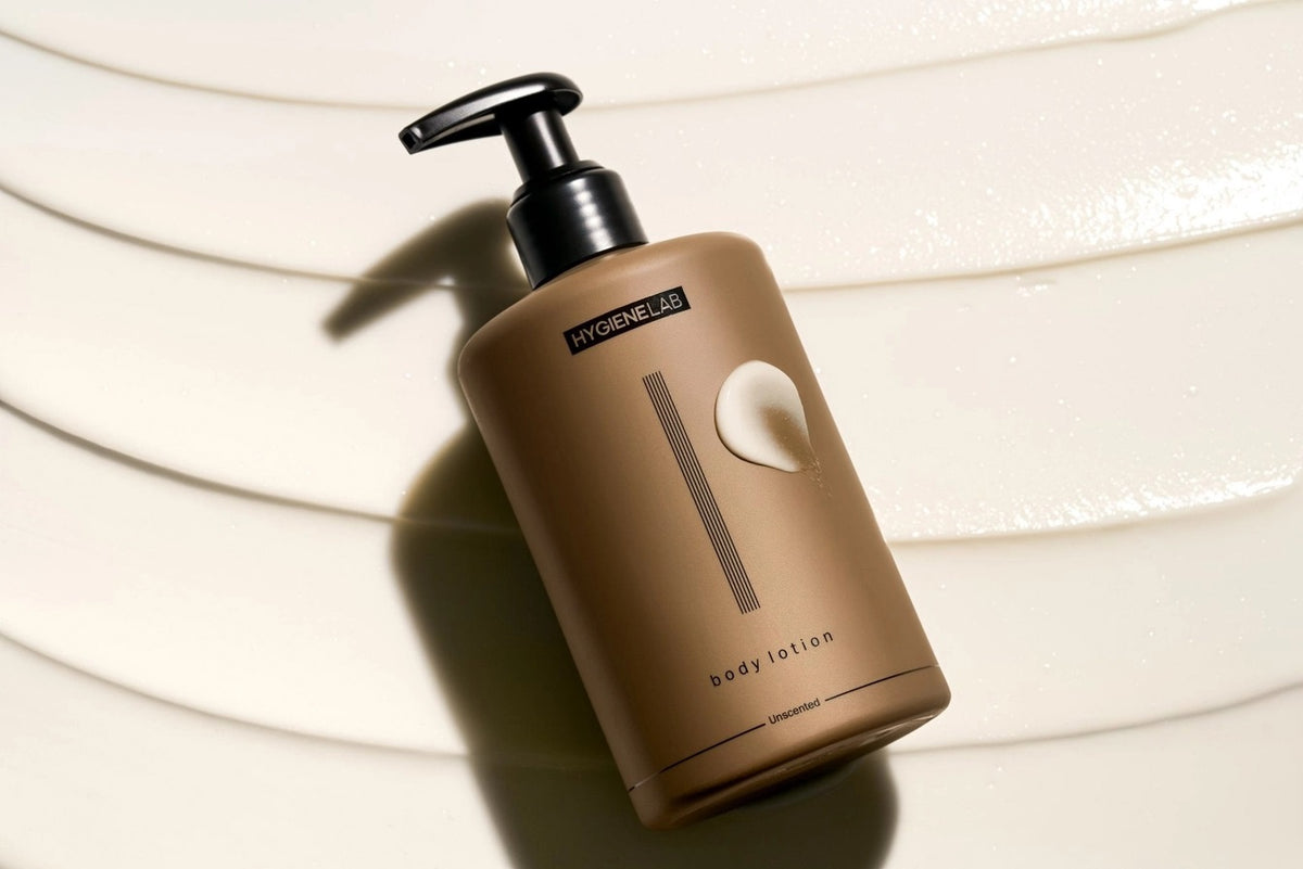 A four-part image showcases the HYGIENELAB - BODY LOTION, UNSCENTED, spotlighting key ingredients Tocopherol, Squalane, and Aloe Barbadensis along with their skin benefits. The composition features a “Clean Non-Toxic Formula” bottle from HYGIENELAB bearing a health certification badge. This dermatologist-approved body lotion is also EWG Verified, ensuring your peace of mind.
