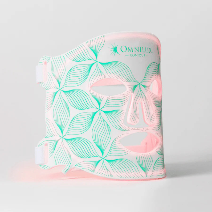 The OMNILUX - CONTOUR FACE MASK by OMNILUX, designed for skin rejuvenation and anti-aging, features red light therapy technology. It has adjustable straps, cutouts for eyes, nose, mouth, and a geometric green-white pattern on a plain white background.