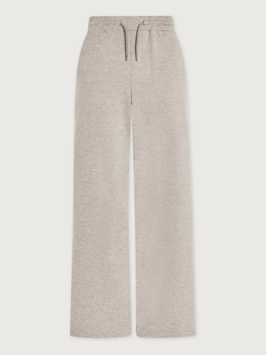 A woman wearing a light gray Varley Motion Easy Jogger 30 in Pebble Marl tank top and matching wide-leg joggers with athletic shoes.