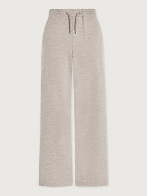 A woman wearing a light gray Varley Motion Easy Jogger 30 in Pebble Marl tank top and matching wide-leg joggers with athletic shoes.