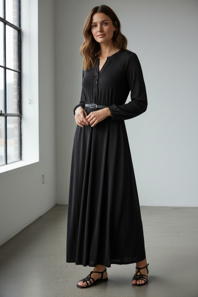 A woman wearing the MOMONI - AMEDE DRESS IN LUREX JERSEY and a black wide-brimmed hat stands in an ornately decorated room with large mirrors and intricate wall designs.