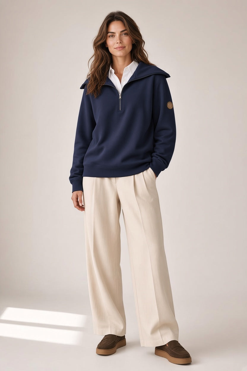 A person wears a SAVE THE DUCK - HINATA HALF ZIP TOP IN NAVY over a white collared shirt, paired with cream-colored wide-leg trousers and brown loafers.