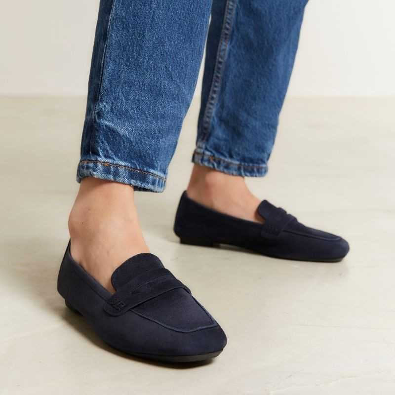 Six pairs of REQINS HEMA suede loafers in marine, featuring a classic penny loafer design and timeless silhouette, are displayed on a light tan surface in various blue and green shades.