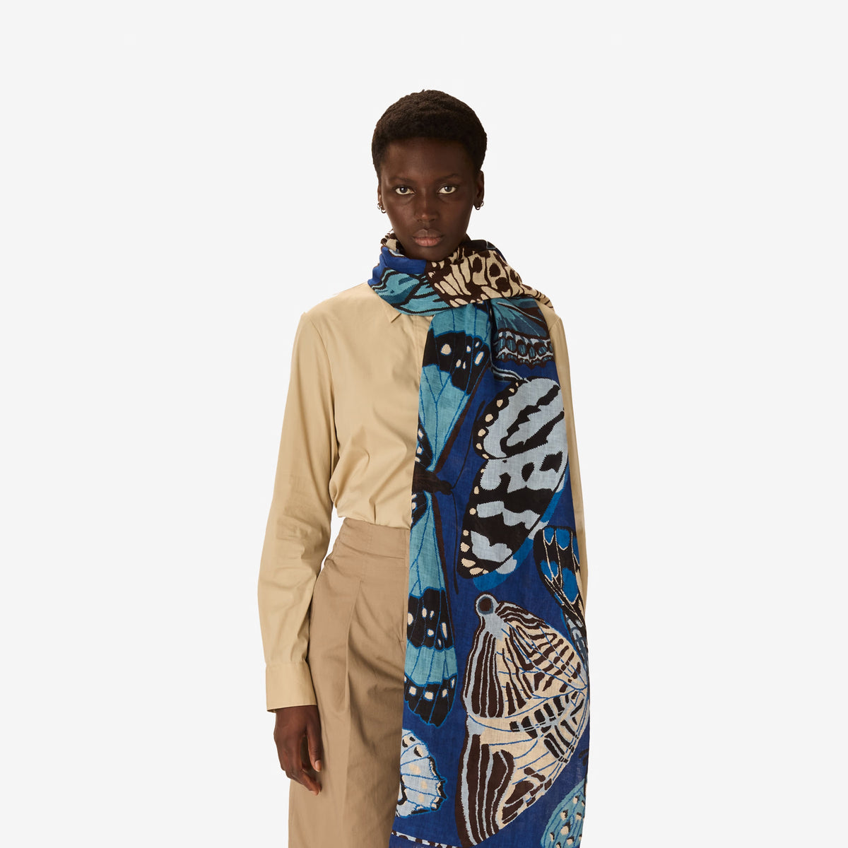 The INOUI EDITIONS - PAPILLON SCARF IN NAVY by INOUI showcases a hand-printed butterfly pattern in blue, white, and tan on navy linen, adding an elegant touch to any outfit.