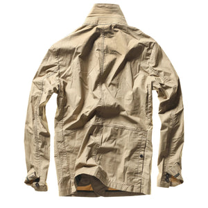A person wears the RELWEN Flyweight Flex Blazer in British Khaki over a blue and white checkered shirt with green pants, standing hands-in-pockets against a white background. Face not visible.