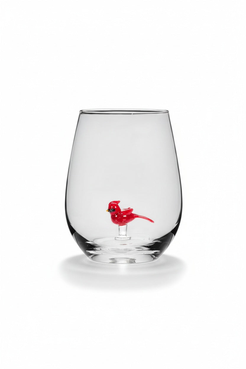 An ABBOTT CARDINAL STEMLESS WINE GLASS featuring a small red bird figure inside, sitting next to a plate of cubed cheese and holly berries.