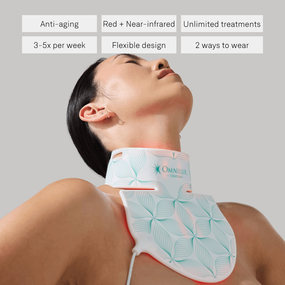 An OMNILUX - CONTOUR NECK & DECOLLETE KIT device by OMNILUX, featuring a white and pink pattern and designed for red light therapy, stands upright on a white surface with soft red light glowing around its edges.