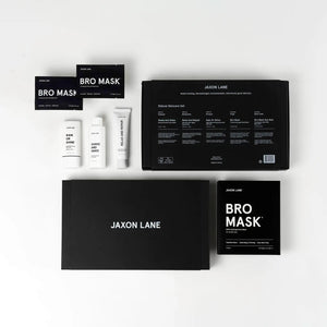 The JAXON LANE - DELUXE SKINCARE SET FOR MEN by JAXON LANE includes the BRO MASK, Rain or Shine sunscreen, Shake and Wake, and two large black boxes, all displayed neatly on a white surface.