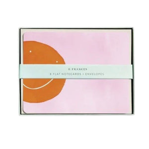 E. FRANCES PAPER’s "Flat Notes Orange Smiley" set features a simple orange smiley face on pink, paired with a plain white envelope—ideal for sending illustrated notecards or thoughtful, handwritten notes.