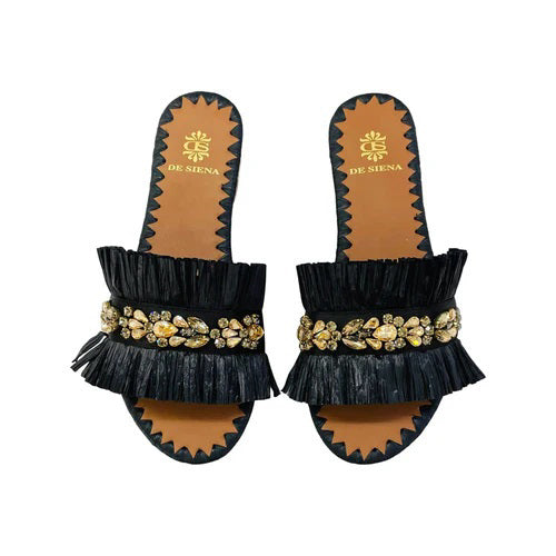 Introducing the DA SIENA Raffia Slides with Crystals from DE SIENA, a stylish pair of summer flats featuring a tan sole and dark blue ruffle strap adorned with intricate gold, pearl, and diamond embellishments in a floral pattern. The edge of the sole boasts a zigzag design in matching dark blue.